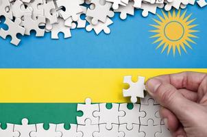 Rwanda flag  is depicted on a table on which the human hand folds a puzzle of white color photo