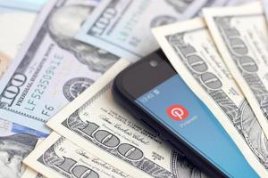 KHARKIV, UKRAINE - MAY 2, 2021 Smartphone screen with Pinterest app and lot of hundred dollar bills. Business and social networking concept photo