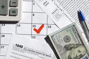 1040 declaración de impuestos sobre la renta individual en blanco con billetes de dólar, calculadora y bolígrafo en la página del calendario con el 15 de abril marcado foto