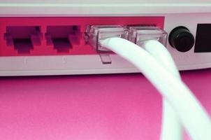 The Internet cable plugs are connected to the Internet router, which lies on a bright pink background. Items required for Internet photo