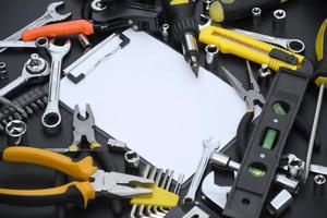 Handyman tool kit on black wooden table with copy space in blank paper tablet. Many wrenches and screwdrivers, pilers and other tools for any types of repair or construction works photo