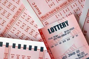 Red lottery ticket lies on pink gambling sheets with numbers for marking to play lottery. Lottery playing concept or gambling addiction. Close up photo