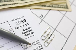 IRS Form W-2G Certain Gambling Winning blank lies with pen and many hundred dollar bills on calendar page photo