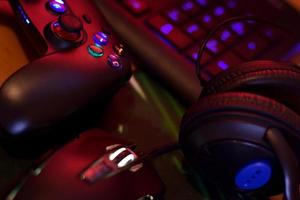 Modern gamepad and gaming mouse lies with keyboard and headphones on table in dark playroom scene. Background composition for video gaming and esports design photo