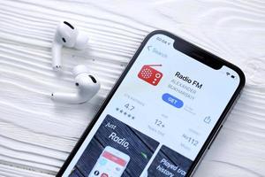 kharkov, ucrania - 5 de marzo de 2021 icono de radio fm y aplicación de la tienda de aplicaciones en la pantalla de visualización del iphone 12 pro con airpods pro en la mesa blanca foto