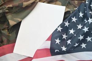 Blank paper lies on United States of America flag and folded military uniform jacket. Military symbols conceptual background banner and copy space photo