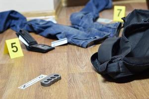 Crime scene investigation - numbering of evidences after the murdering in apartment. Brass knuckle, wallet and clothes with evidence markers photo