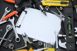 Handyman tool kit on black wooden table with copy space in blank paper tablet. Many wrenches and screwdrivers, pilers and other tools for any types of repair or construction works photo