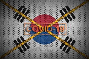 bandera de corea del sur y sello covid-19 con cruz de cinta de borde de cuarentena naranja. coronavirus o concepto de virus 2019-ncov foto