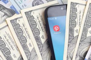 KHARKIV, UKRAINE - MAY 2, 2021 Smartphone screen with Pinterest app and lot of hundred dollar bills. Business and social networking concept photo