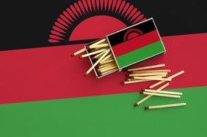 Malawi flag  is shown on an open matchbox, from which several matches fall and lies on a large flag photo