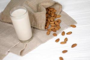 Glass of almond milk with almond nuts on canvas fabric on white wooden table. Dairy alternative milk for detox, healthy eating and diets photo