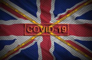 Great britain flag and Covid-19 stamp with orange quarantine border tape cross. Coronavirus or 2019-nCov virus concept photo