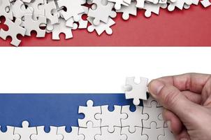 Netherlands flag  is depicted on a table on which the human hand folds a puzzle of white color photo