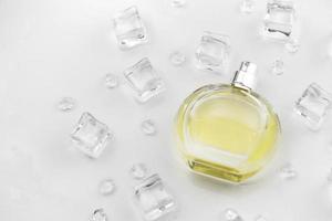 Female perfume yellow bottle, Objective photograph of perfume bottle in ice cubes and water on white table. View from above. Mockup product photo, concept of freshness photo