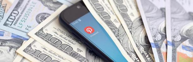 KHARKIV, UKRAINE - MAY 2, 2021 Smartphone screen with Pinterest app and lot of hundred dollar bills. Business and social networking concept photo