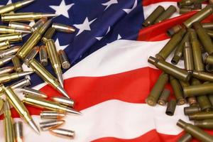 Many yellow 9mm and 5.56mm bullets and cartridges on United States flag. Concept of gun trafficking on USA territory or shooting range photo