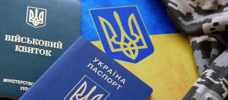 Ukrainian military ID and foreign passport on fabric with texture of pixeled camouflage. Cloth with camo pattern in grey, brown and green shapes with Ukrainian army personal token and passport. photo