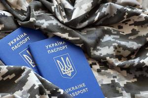 Ukrainian foreign passport on fabric with texture of military pixeled camouflage. Cloth with camo pattern in grey, brown and green pixel shapes and Ukrainian ID photo