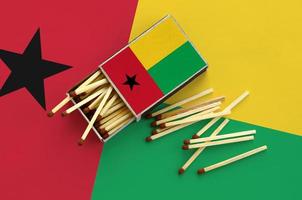 Guinea Bissau flag  is shown on an open matchbox, from which several matches fall and lies on a large flag photo