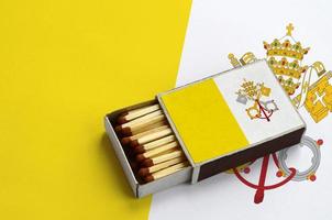 Vatican City State flag  is shown in an open matchbox, which is filled with matches and lies on a large flag photo