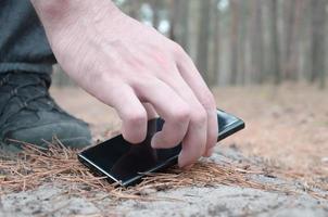 Male hand picking up lost mobile phone from a ground in autumn fir wood path. The concept of finding a valuable thing and good luck photo