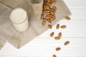 Glass of almond milk with almond nuts on canvas fabric on white wooden table. Dairy alternative milk for detox, healthy eating and diets photo