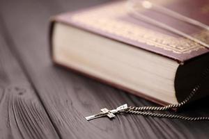 Silver necklace with crucifix cross on christian holy bible book on black wooden table. Asking blessings from God with the power of holiness, which brings luck photo