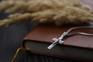 collar de plata con cruz crucifijo en el libro de la santa biblia cristiana sobre una mesa de madera negra. pidiendo bendiciones de dios con el poder de la santidad foto