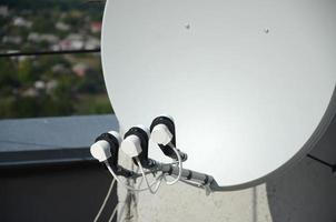 White satellite dish with three converters mounted on residental building rooftop concrete wall. Satellite television photo