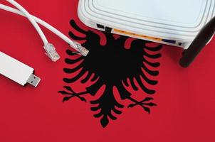 Albania flag depicted on table with internet rj45 cable, wireless usb wifi adapter and router. Internet connection concept photo