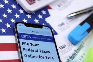 KHARKOV, UKRAINE - MARCH 5, 2021 Official IRS website on iPhone 12 pro screen with 1040 and w-2 paper tax forms on US flag photo