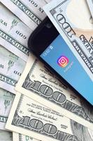 KHARKIV, UKRAINE - MAY 2, 2021 Smartphone screen with Instagram app and lot of hundred dollar bills. Business and social networking concept photo