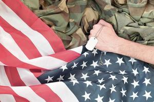 Male hand holds dog tag on USA flag and military uniform background photo