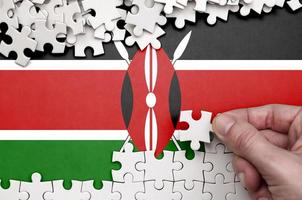 Kenya flag  is depicted on a table on which the human hand folds a puzzle of white color photo