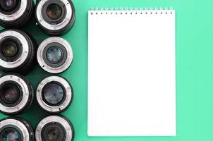 Several photographic lenses and white notebook lie on a bright turquoise background. Copy space photo