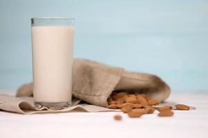 Glass of almond milk with almond nuts on canvas fabric on white wooden table. Dairy alternative milk for detox, healthy eating and diets photo