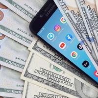 KHARKIV, UKRAINE - MAY 2, 2021 Smartphone screen with many popular apps and lot of hundred dollar bills. Business and social networking concept photo