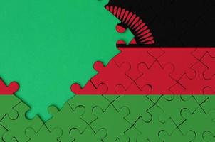 Malawi flag  is depicted on a completed jigsaw puzzle with free green copy space on the left side photo