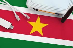 Suriname flag depicted on table with internet rj45 cable, wireless usb wifi adapter and router. Internet connection concept photo