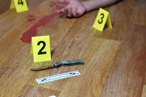 investigación de la escena del crimen - cuchillo ensangrentado y mano de la víctima con marcadores criminales amarillos en el piso de la cocina foto