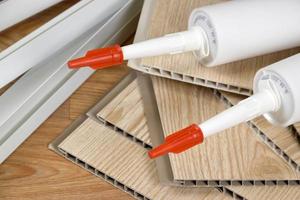 Set of items for PVC ceiling indoor works. Assembly adhesive bottles and PVC panels with plastic corners. Indoor VPC siding kit. Interior renovation works or construction photo