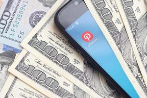 KHARKIV, UKRAINE - MAY 2, 2021 Smartphone screen with Pinterest app and lot of hundred dollar bills. Business and social networking concept photo