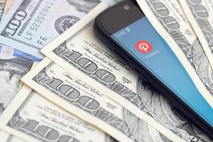 KHARKIV, UKRAINE - MAY 2, 2021 Smartphone screen with Pinterest app and lot of hundred dollar bills. Business and social networking concept photo
