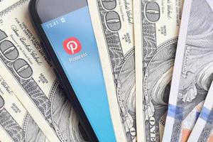 KHARKIV, UKRAINE - MAY 2, 2021 Smartphone screen with Pinterest app and lot of hundred dollar bills. Business and social networking concept photo