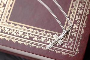 Silver necklace with crucifix cross on christian holy bible book on black wooden table. Asking blessings from God with the power of holiness, which brings luck photo