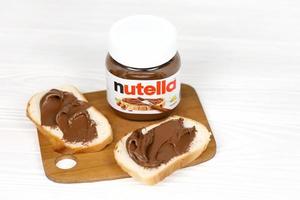 kharkov, ucrania - 27 de diciembre de 2020 lata de vidrio de nutella y untada en pan recién horneado. nutella es fabricada por la empresa italiana ferrero introducida por primera vez en 1964 foto