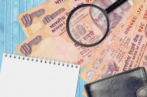 10 Indian rupees bills and magnifying glass with black purse and notepad. Concept of counterfeit money. Search for differences in details on money bills to detect fake photo