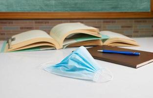 mask and blurred books on table in front of blackboard in classroom photo