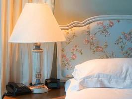 lamp on bedside near telephone, clock and pillow photo